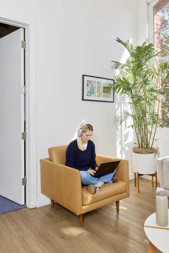 Teammate working on a laptop in a leather armchair by a sunlit office window